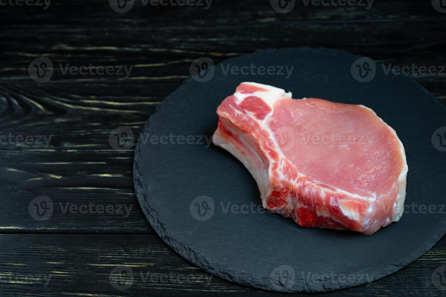 Top view of one pieces raw pork chop steaks on a black stone cutting board. photo