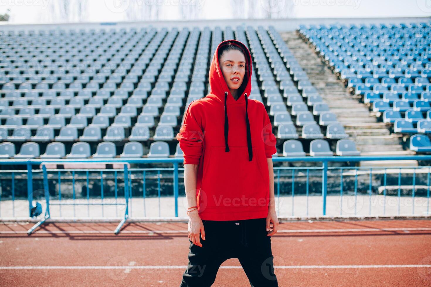 Young sports woman in sweatshirt resting after jogging training on the running track at summer photo