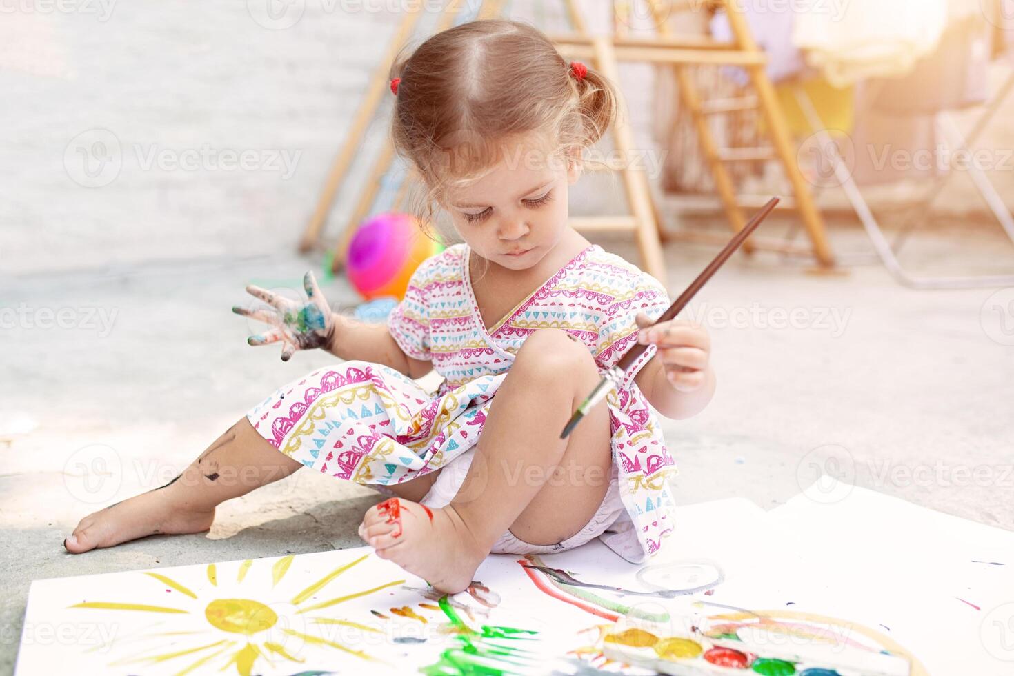 linda pequeño caucásico niña disfrutando pintura a el patio interior con papel, agua color y Arte cepillar. selectivo atención foto