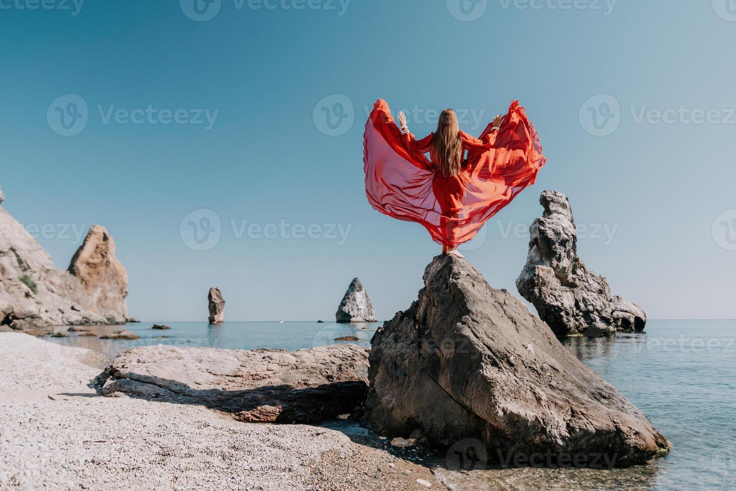 Woman travel sea. Young Happy woman in a long red dress posing on a beach near the sea on background of volcanic rocks, like in Iceland, sharing travel adventure journey photo