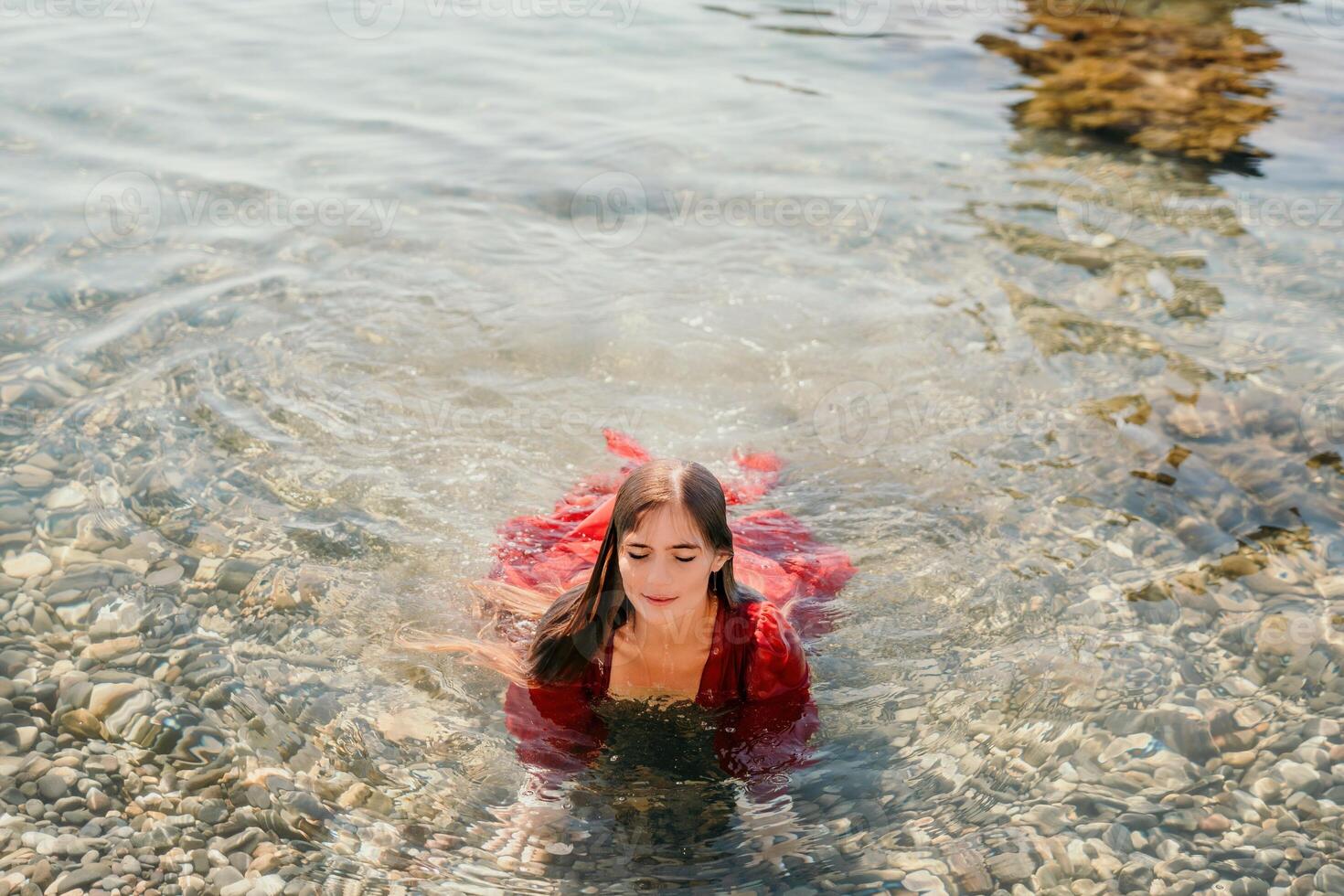 Woman travel sea. Happy tourist in red dress enjoy taking picture outdoors for memories. Woman traveler posing in sea beach, surrounded by volcanic mountains, sharing travel adventure journey photo