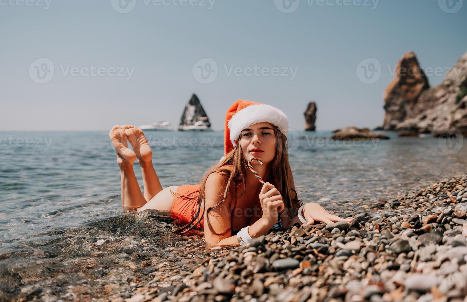 Woman travel sea. Happy tourist enjoy taking picture on the beach for memories. Woman traveler in Santa hat looks at camera on the sea bay, sharing travel adventure journey photo