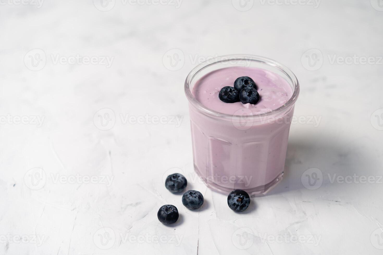 Tasty fresh blueberry yoghurt shake dessert in glass standing on white table background. photo