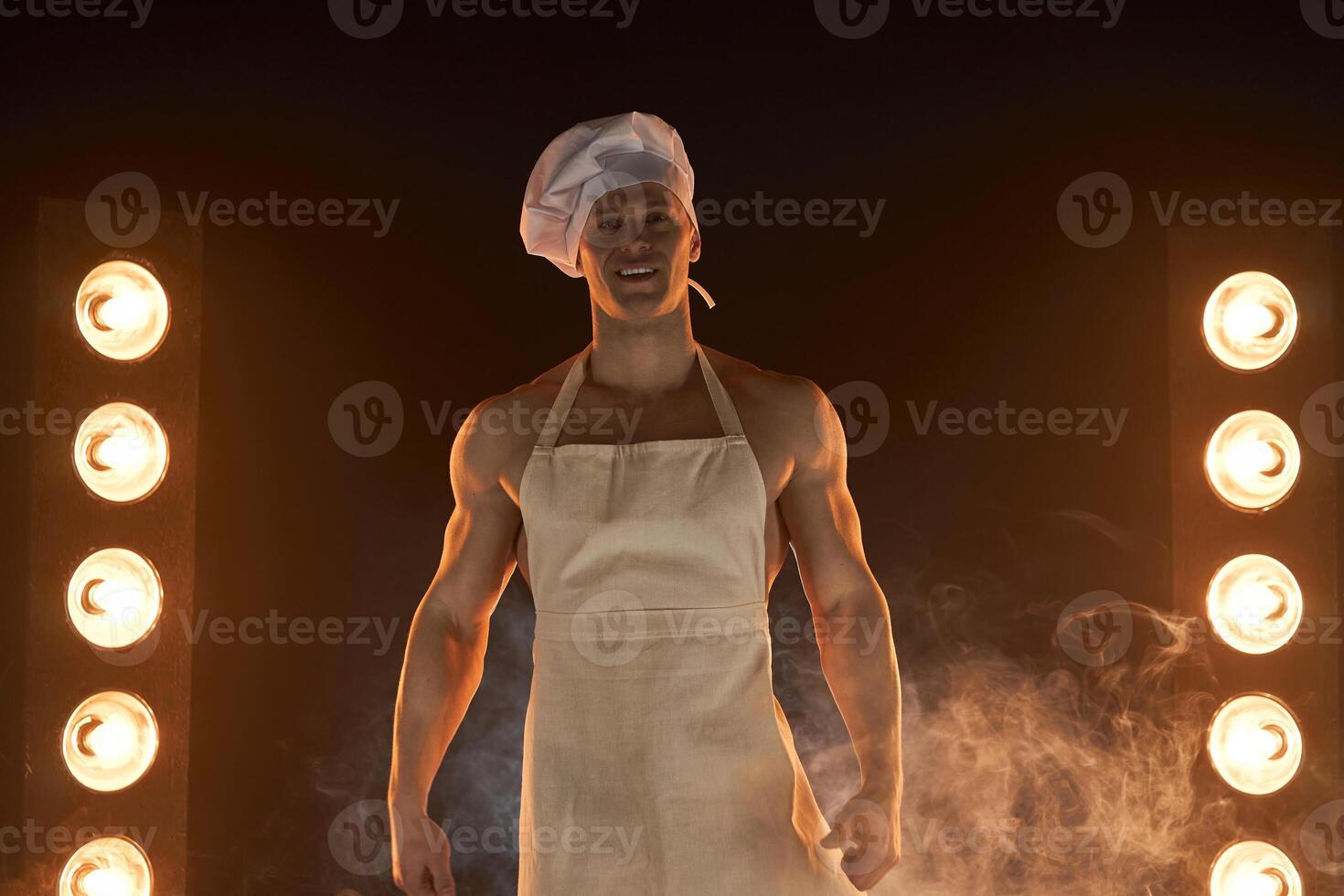 Portrait of muscular chef wearing white apron and cheef hat,  on smoky background photo