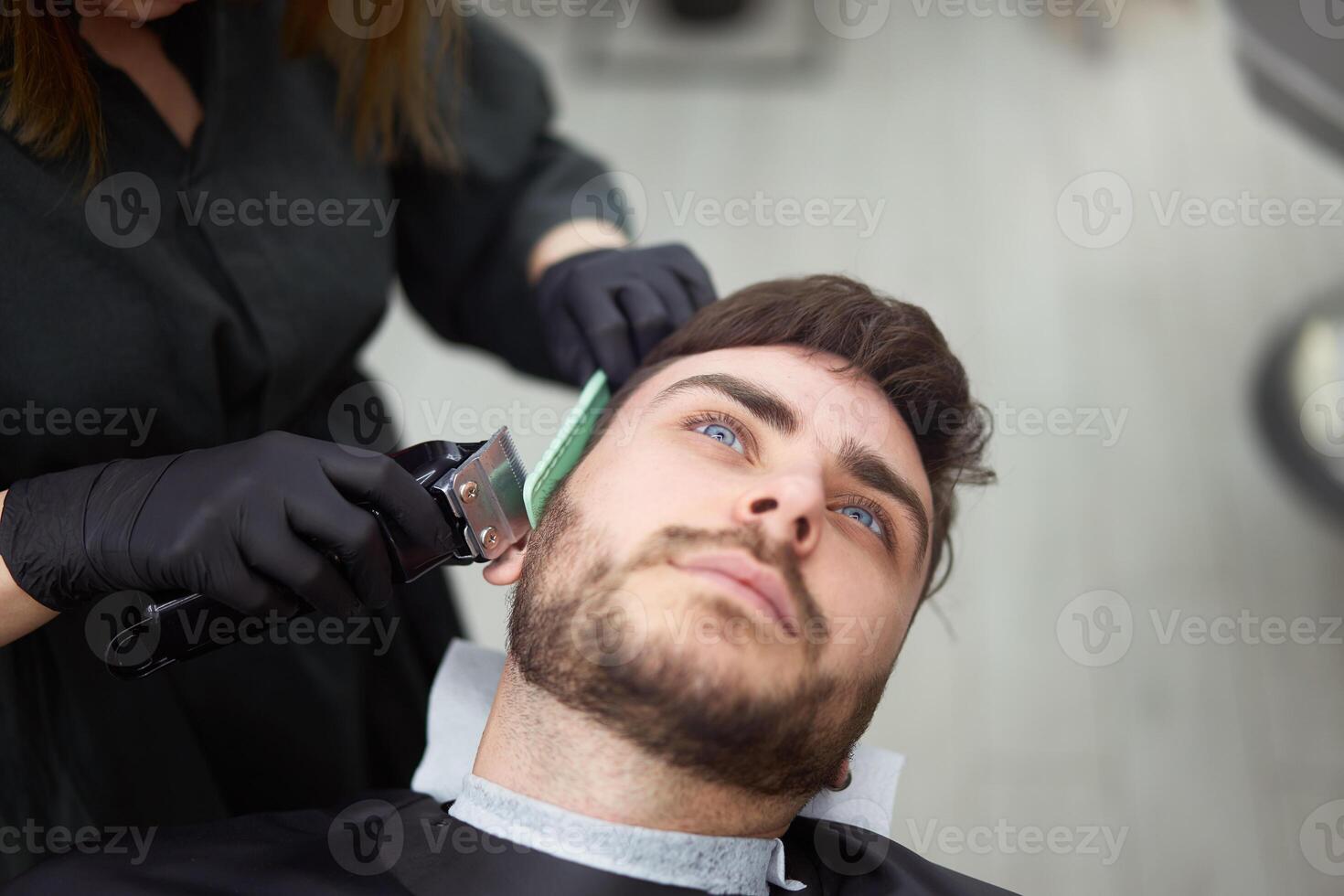 Young beautiful caucasian woman hairdresser cuts beard  handsome man at modern barbershop photo