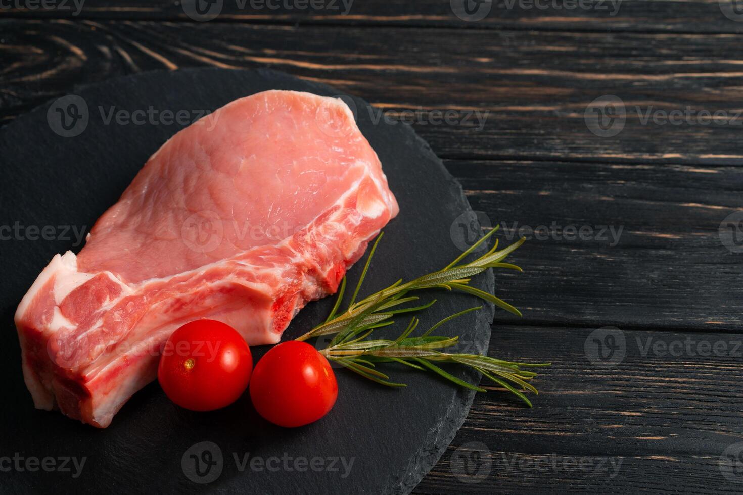 Top view of one pieces raw pork chop steaks with cherry tomatoes on a black stone cutting board. photo