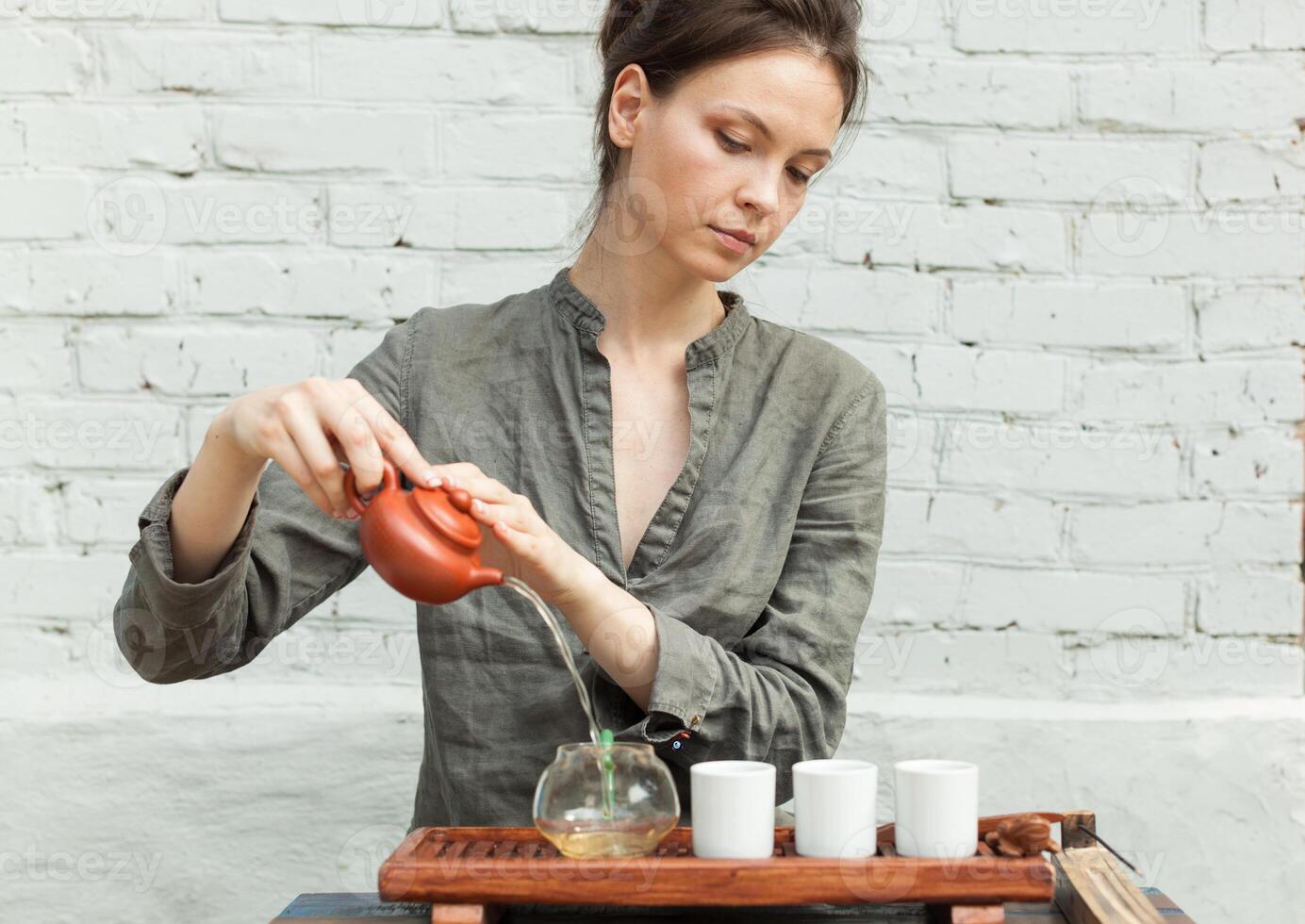 oriental Maestro de té ceremonia con blanco ladrillo pared en el antecedentes. tradicional té fiesta en el naturaleza con mujer vestido en el gris camisa foto