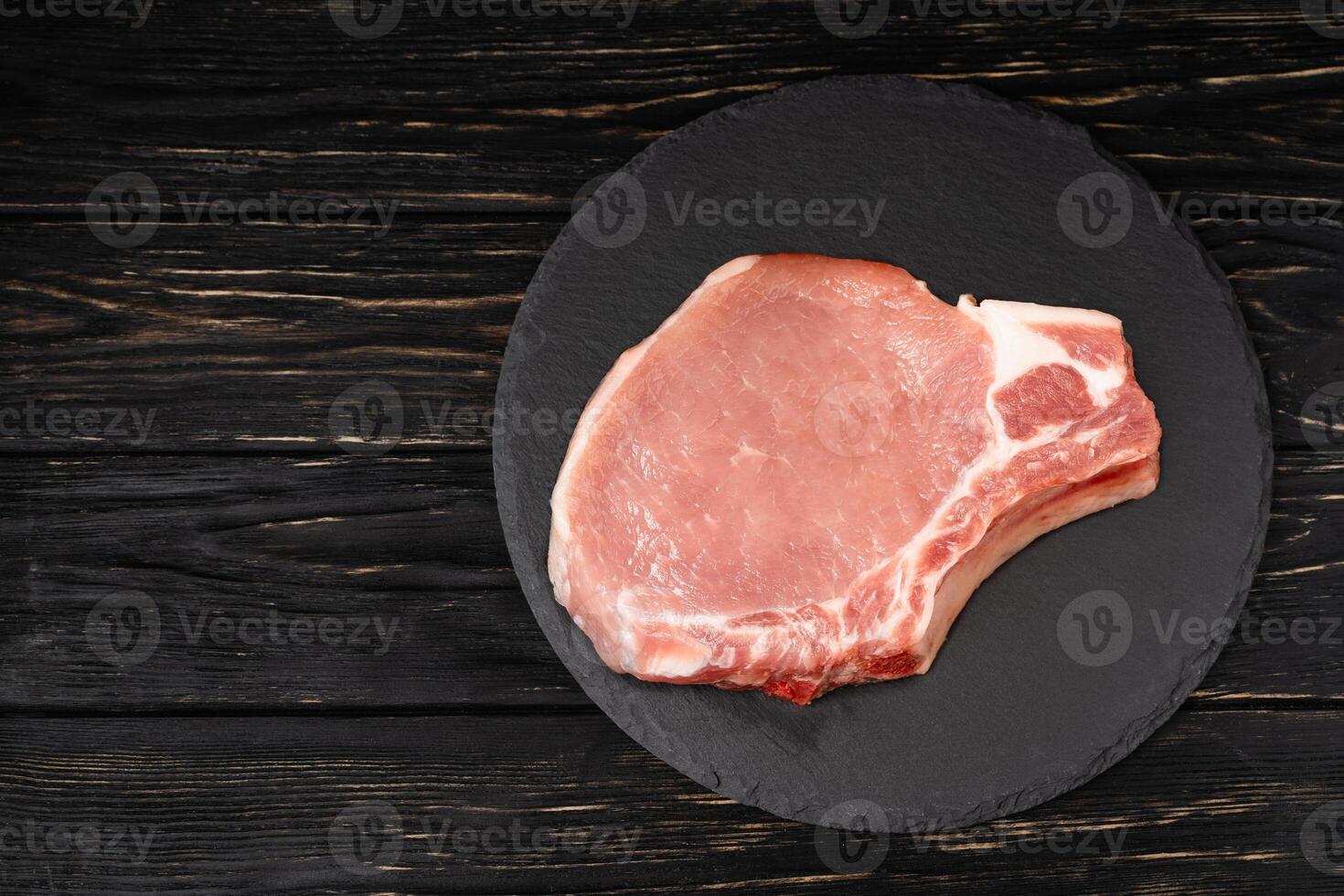 Top view of one pieces raw pork chop steaks on a black stone cutting board. photo