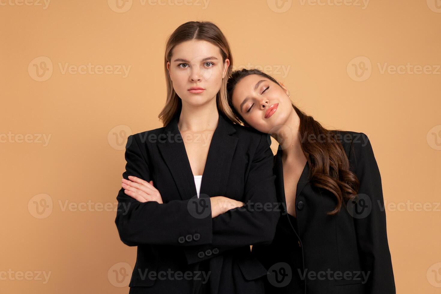 Two young business woman dressed black suit standing studio orange color background photo