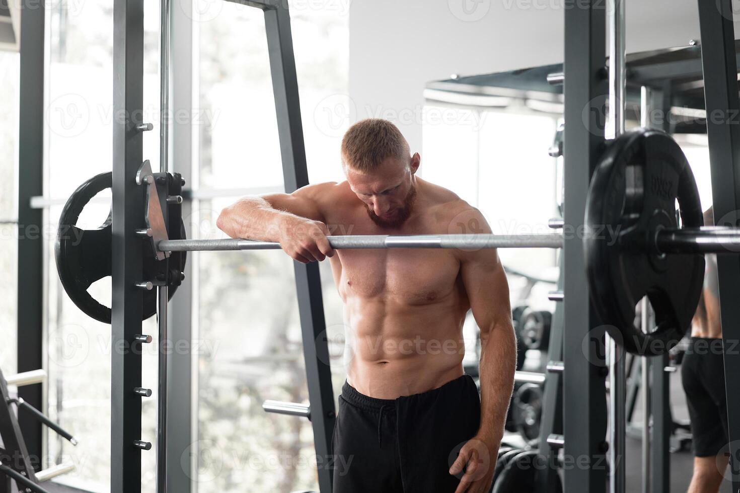 Gym man leaning barbell resting after hard training. Handsome caucasian athlete take break. photo