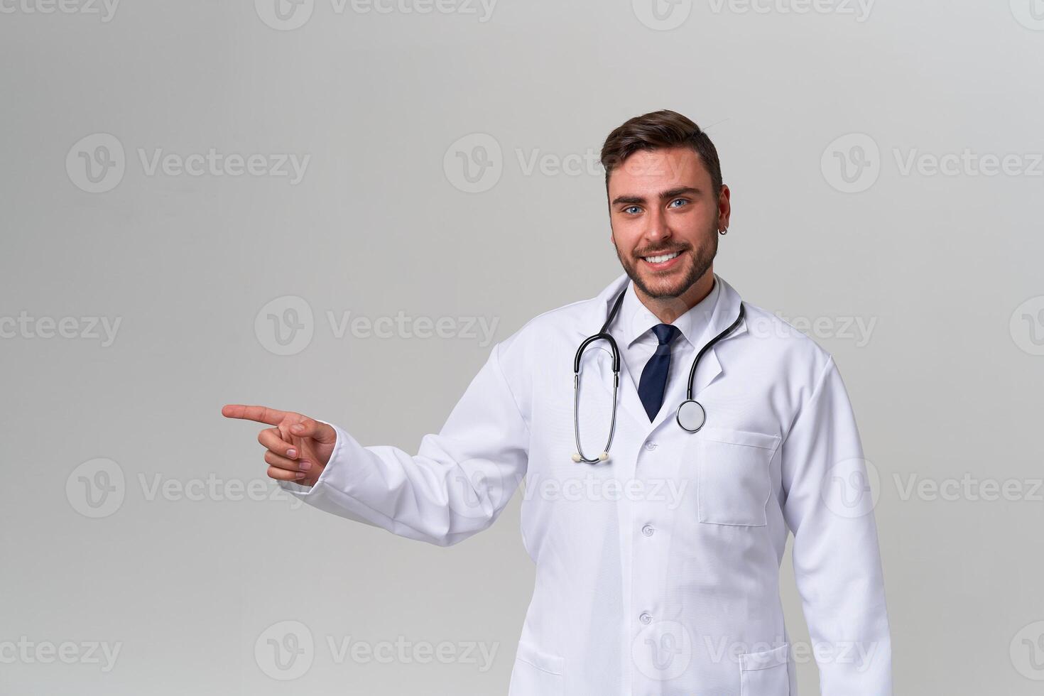 Young handsome modern doctor in a white medical gown stands in the studio on a white background. Student trainee of a medical university. photo