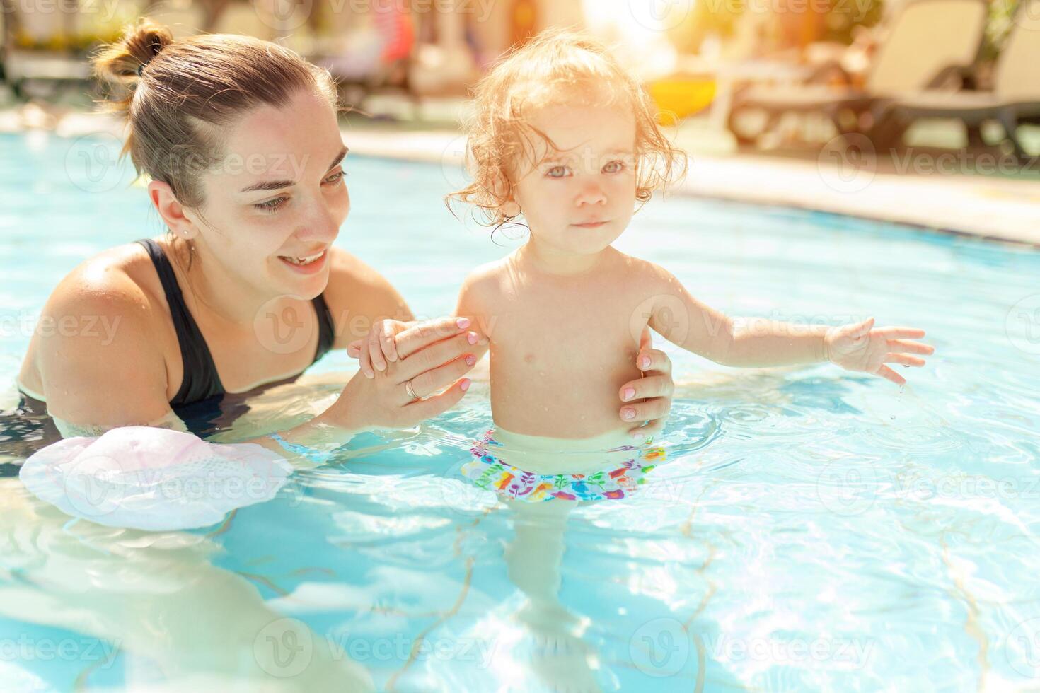 Mom and little daughter are played in the open swimming pool. Family with one child on vacation in warm countries. Positive people on vacation. photo