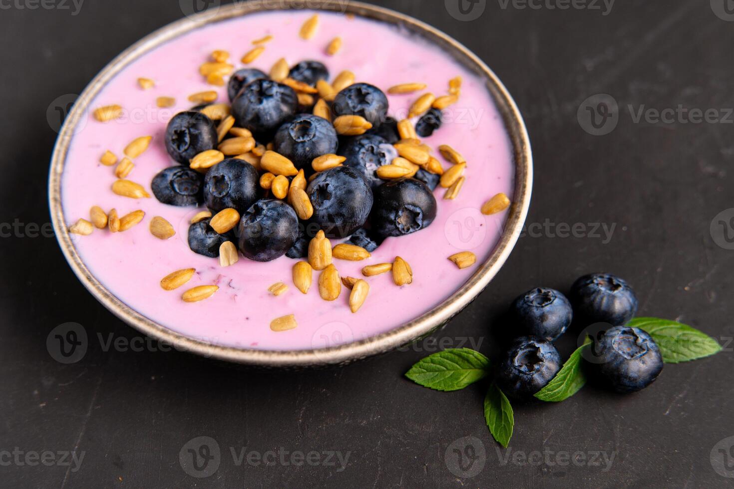 Tasty fresh blueberry yoghurt shake dessert in ceramic bowl standing on black dark table background. photo