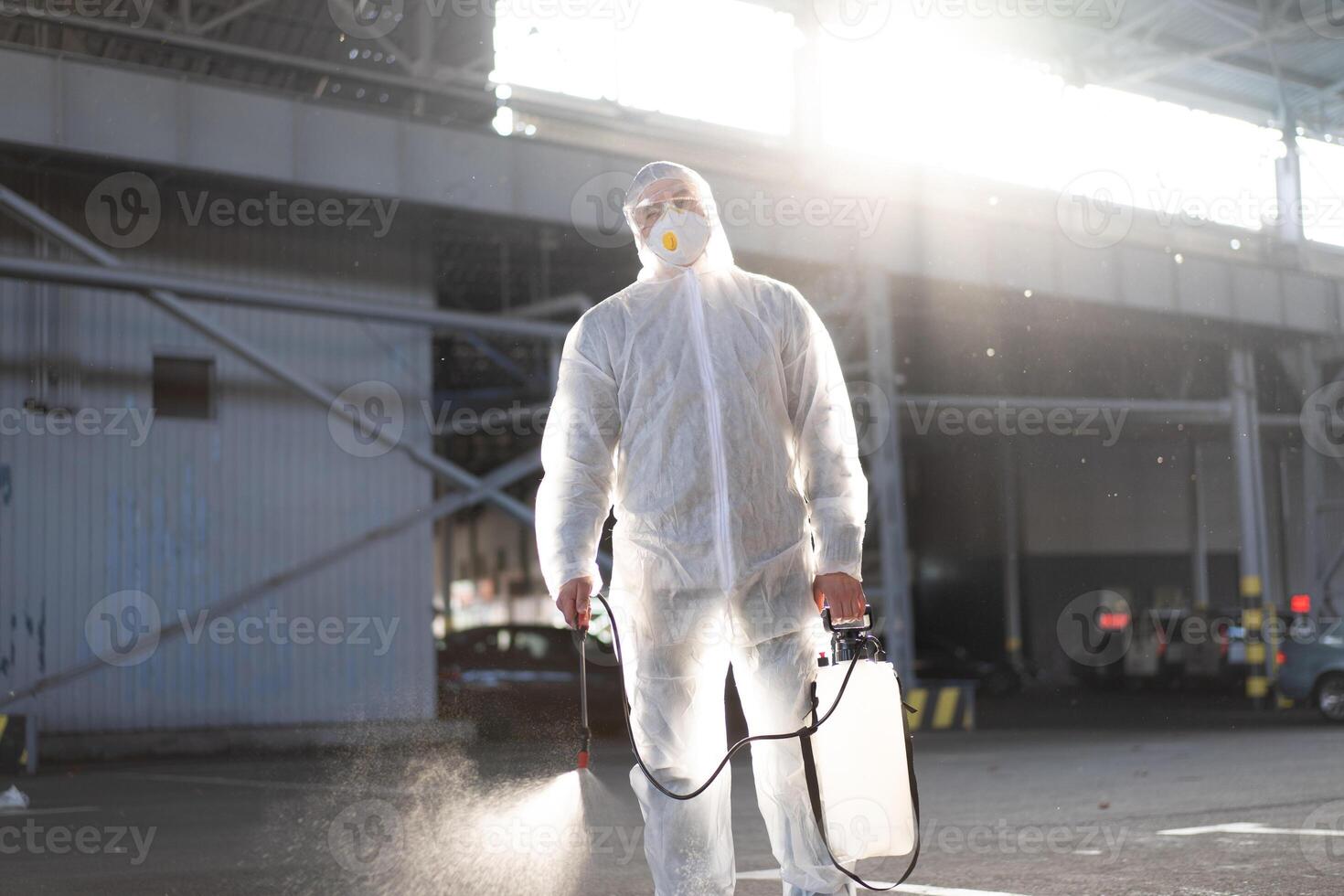 Man dressed white protective overalls spraying surface antibacterial sanitizer sprayer during quarantine photo