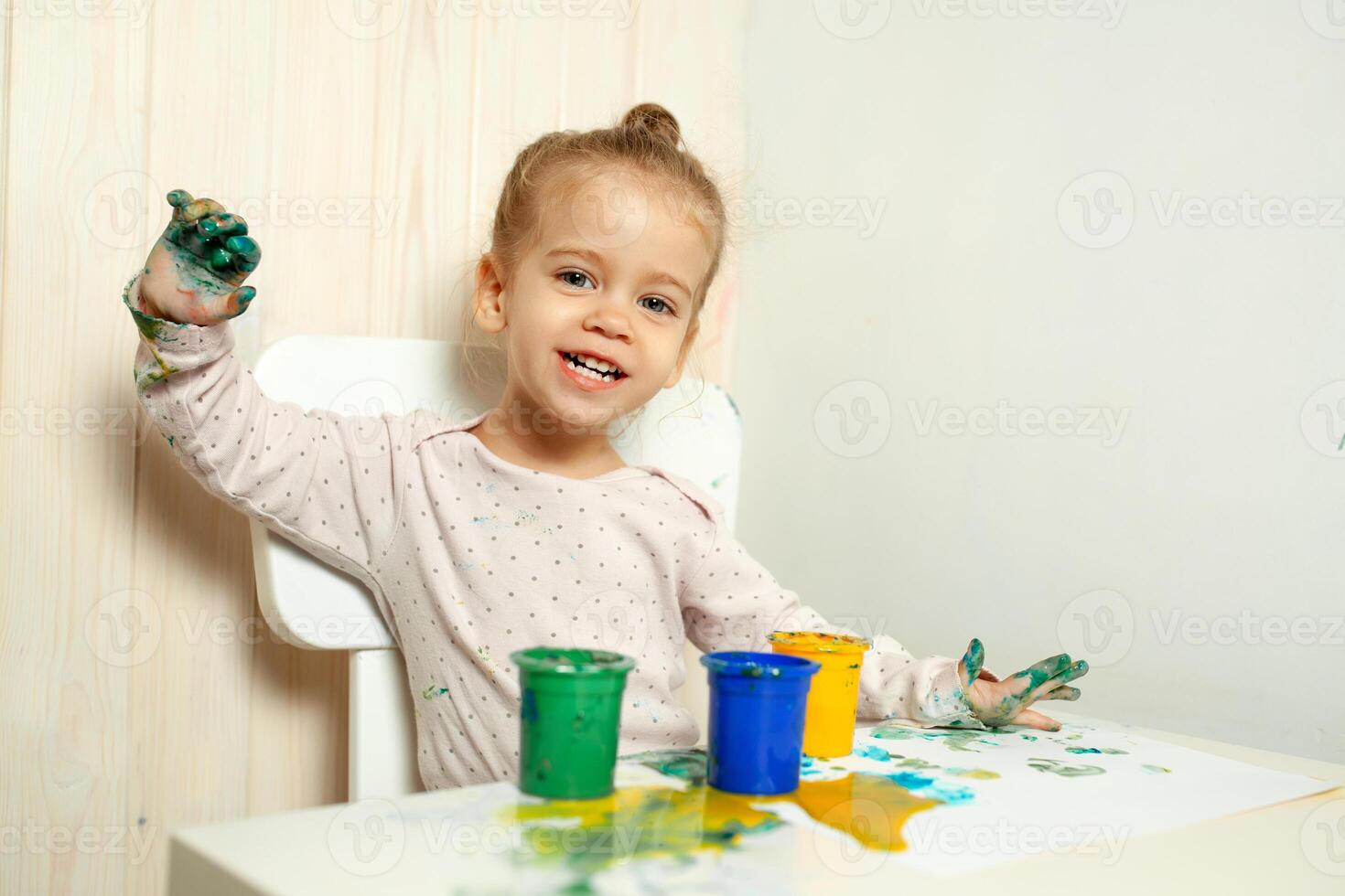 hermosa pequeño niña sorteos con dedo pinturas en un blanco sábana de papel. creativo niño desarrollo en jardín de infancia o gratis hora a hogar foto