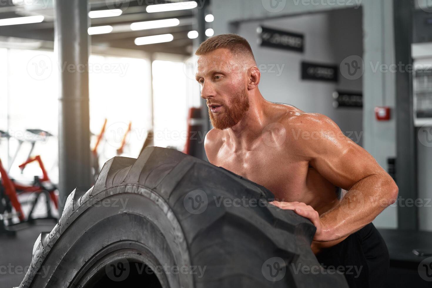 atleta juguetón hombre levantar rueda gimnasio cruzar formación empujar grande neumático medio adulto hermoso deportista carrocero levantador de pesas ideal cuerpo foto