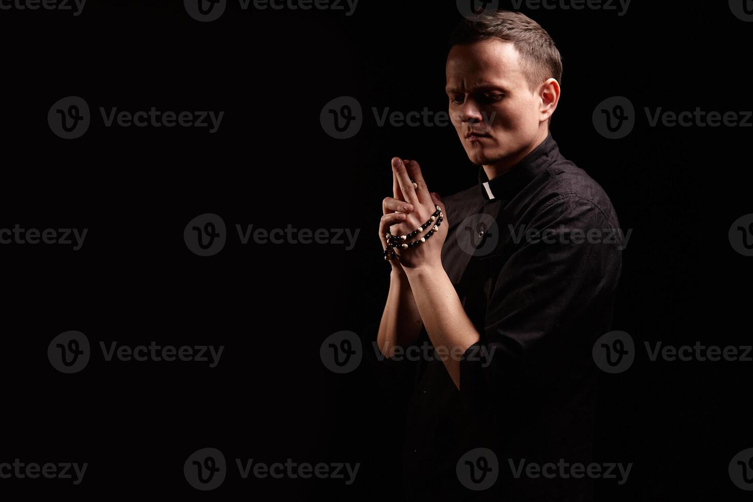 Young adult caucasian catholic priest on dark red background photo