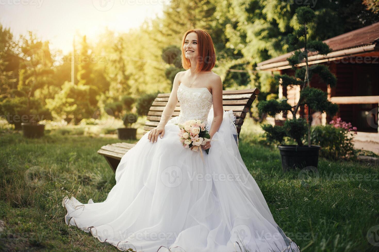 Bride in elegant wedding gown sits on stone bench photo