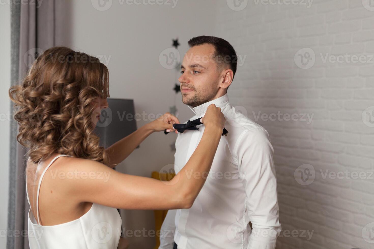 Bride fixes bow tie on groom s neck while they stand photo