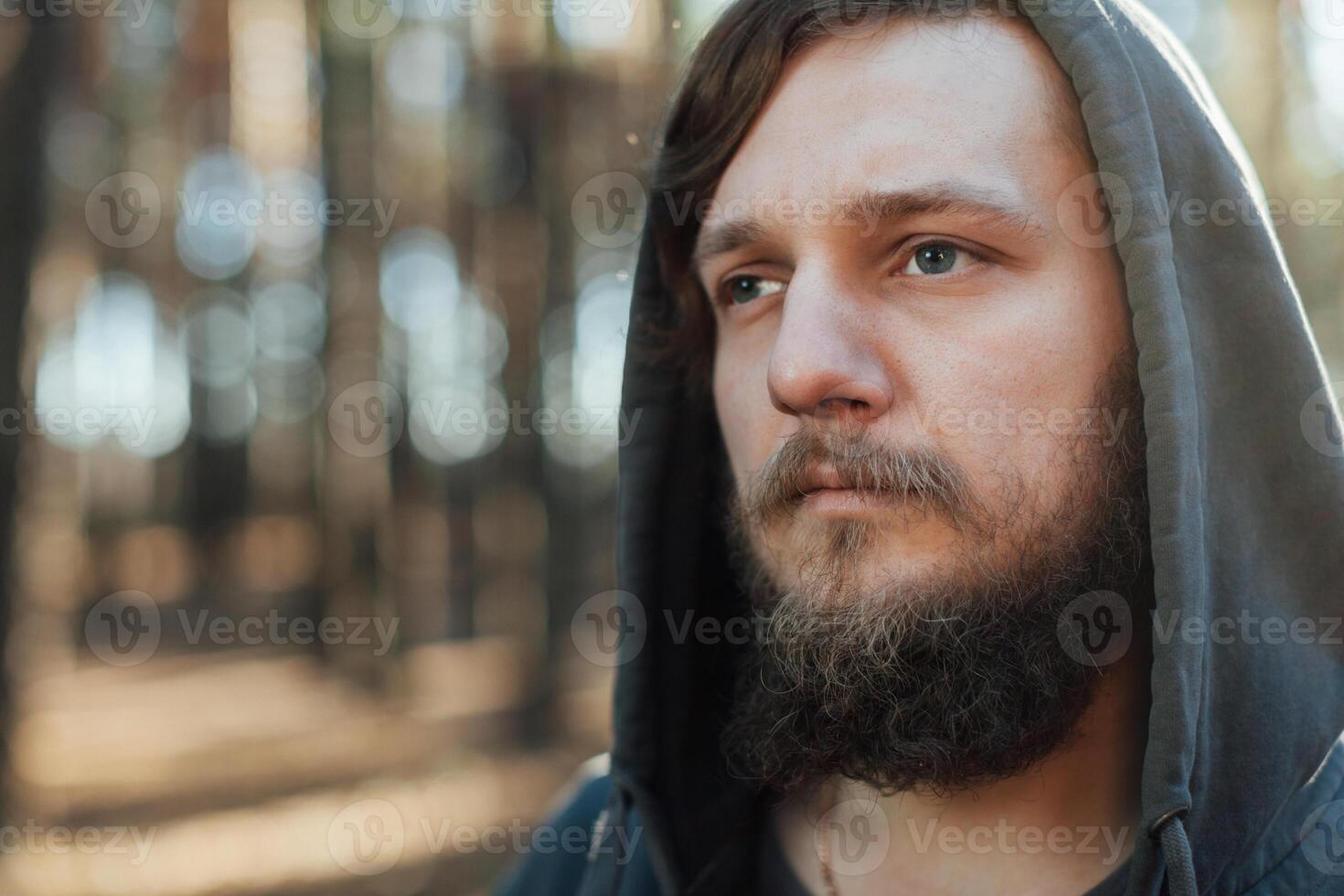 close up portrait of a bearded hipster tourist in gray hood man in the sunlight woods forest photo