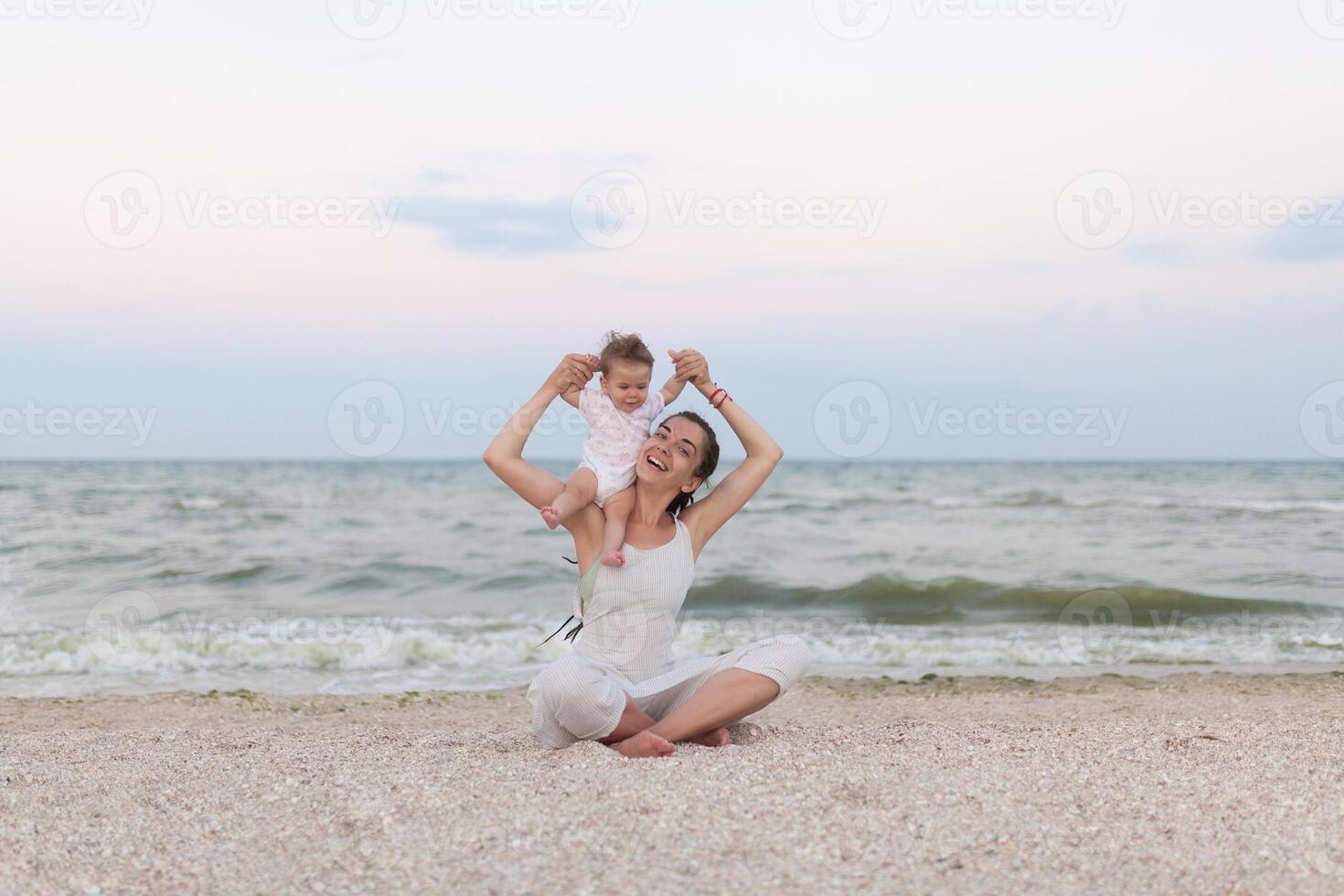 Happy family mother and child daughter doing yoga, meditate in lotus position on beach at sunset photo