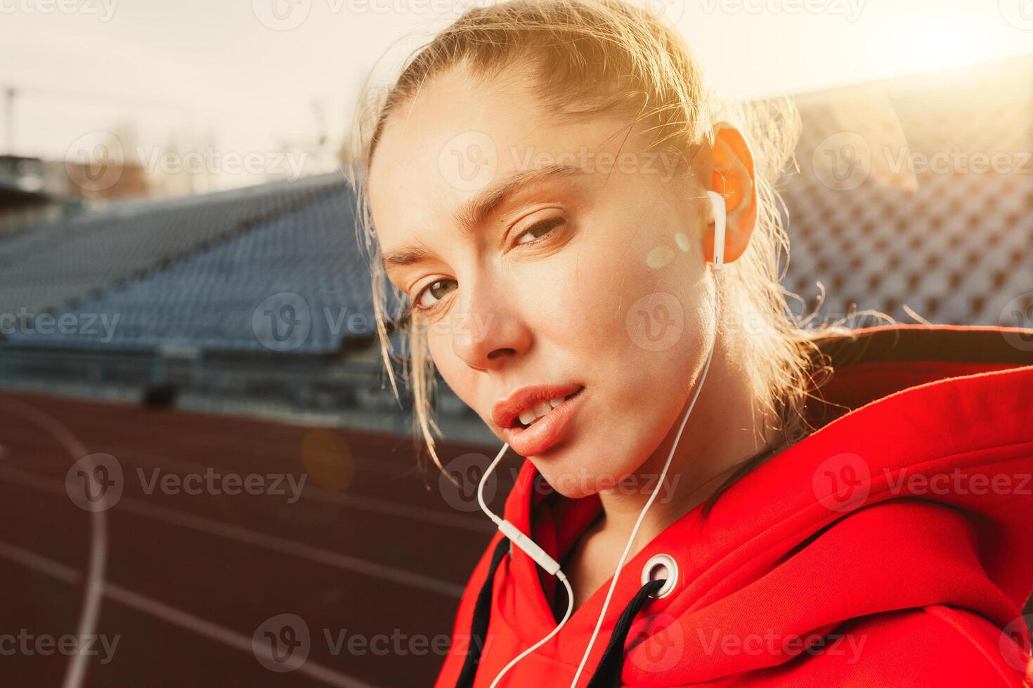 Side view of a young sport woman wearing a red hoodie. He is jogging and listening to music with his smartphone in hands. photo