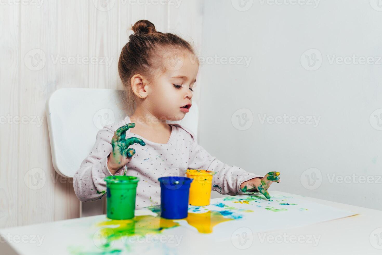 Beautiful little girl draws with finger paints on a white sheet of paper. Creative child development in kindergarten or free time at home photo