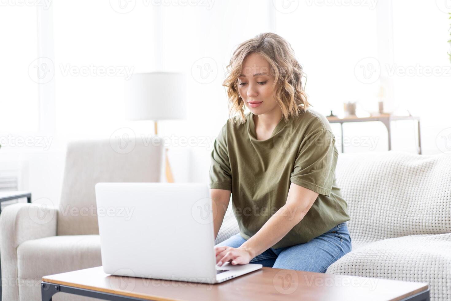 Woman using laptop computer while sitting sofa with big window on background at home interior photo