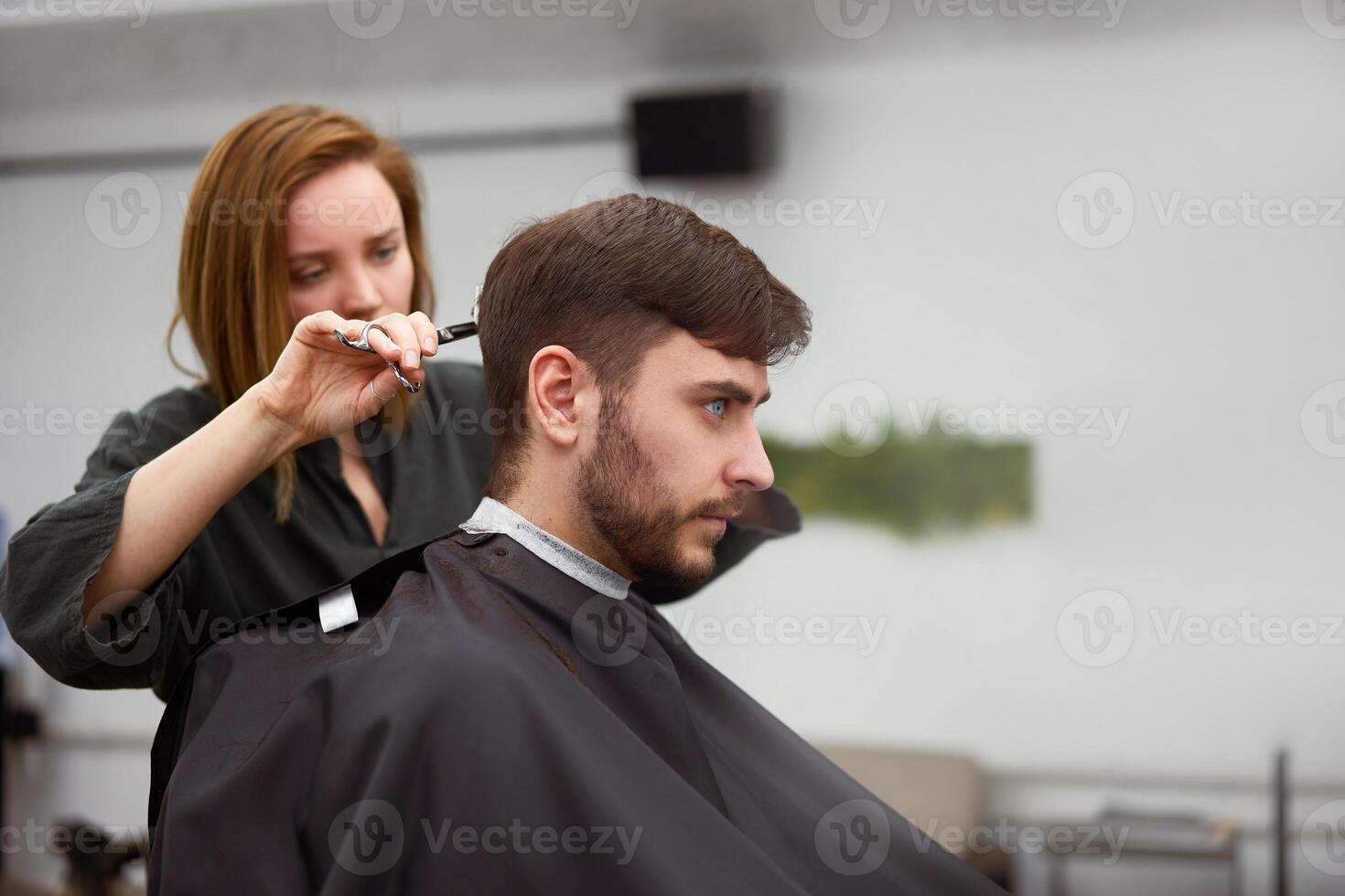 hermoso azul ojos hombre sentado en Barbero tienda. estilista peluquero mujer corte su cabello. hembra Barbero. foto