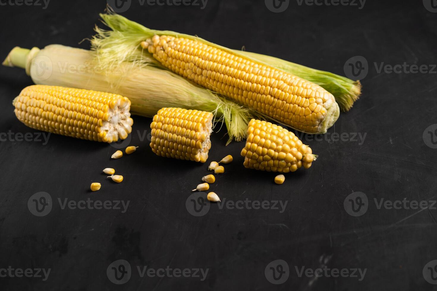 Corn cob with green leaves lies on table black color background. photo