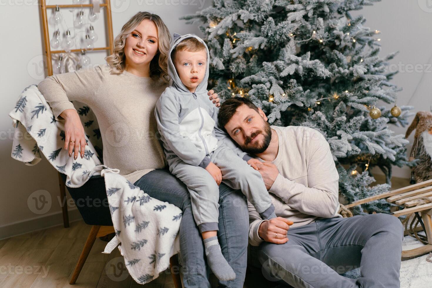 Christmas Family Happiness Portrait of dad, pregnant mom and little son  sitting armchair at home near Christmas tree hug smile photo