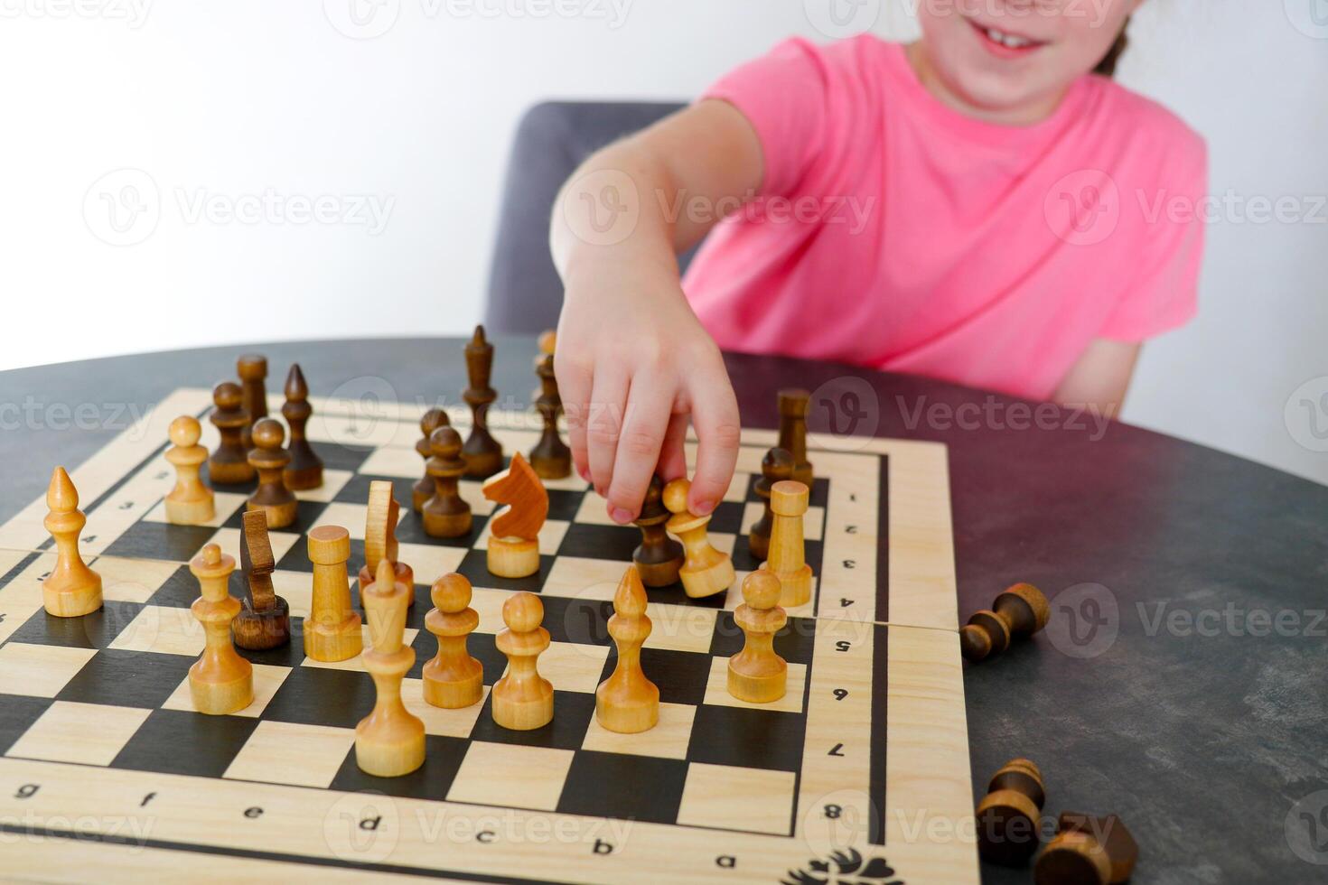 smiling girl makes a move with chess pieces on the board photo