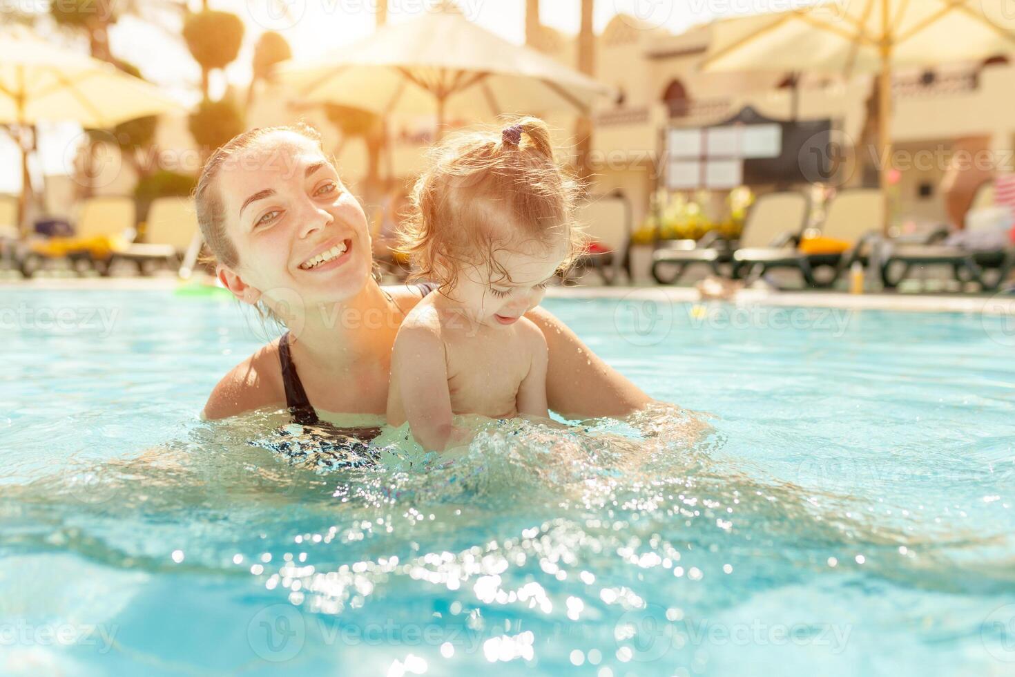 Mom and little daughter are played in the open swimming pool. Family with one child on vacation in warm countries. Positive people on vacation. photo