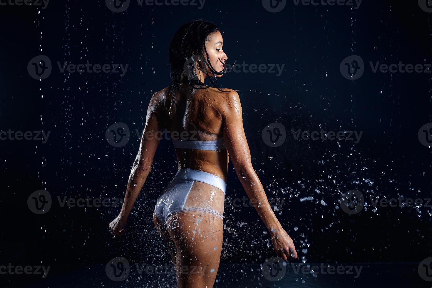 hermosa atlético caucásico niña con un Perfecto figura es en pie debajo el agua. aptitud mujer en un rociar de agua. Deportes frescura. concepto foto