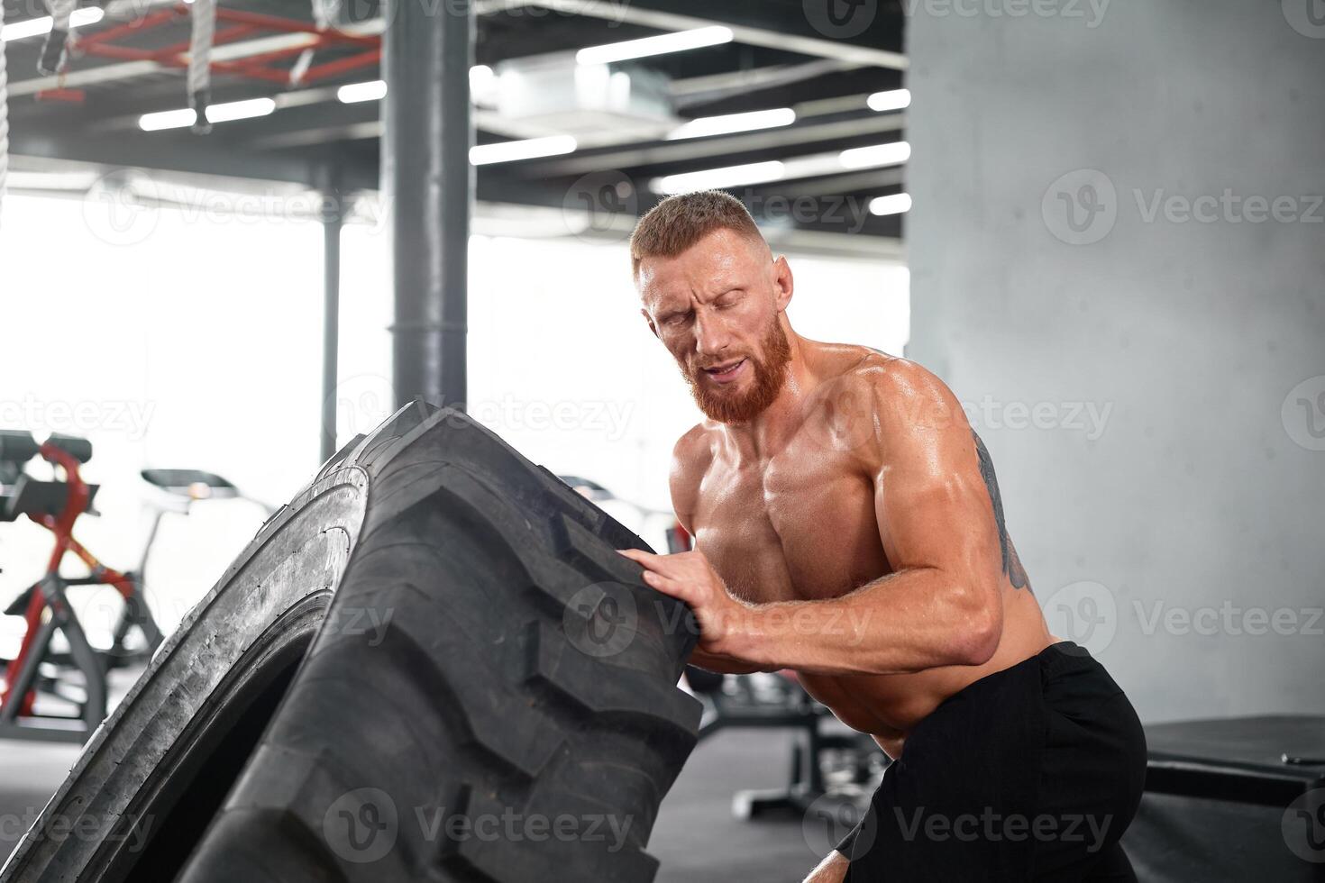 atleta juguetón hombre levantar rueda gimnasio cruzar formación empujar grande neumático medio adulto hermoso deportista carrocero levantador de pesas ideal cuerpo foto