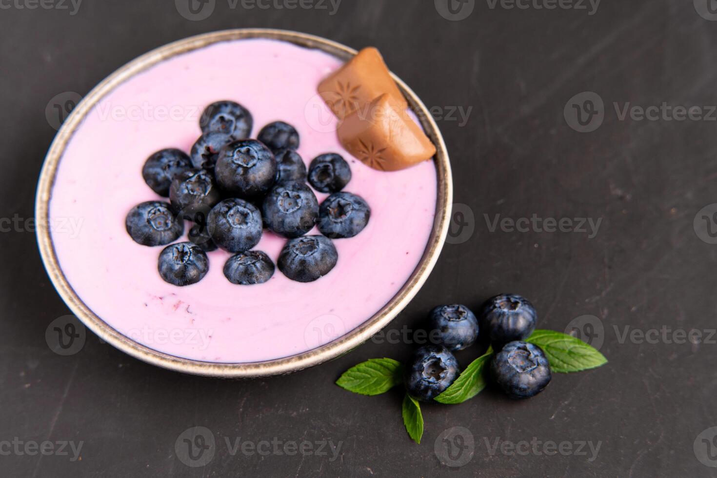 Tasty fresh blueberry yogurt shake dessert in ceramic bowl standing on black dark table background. photo