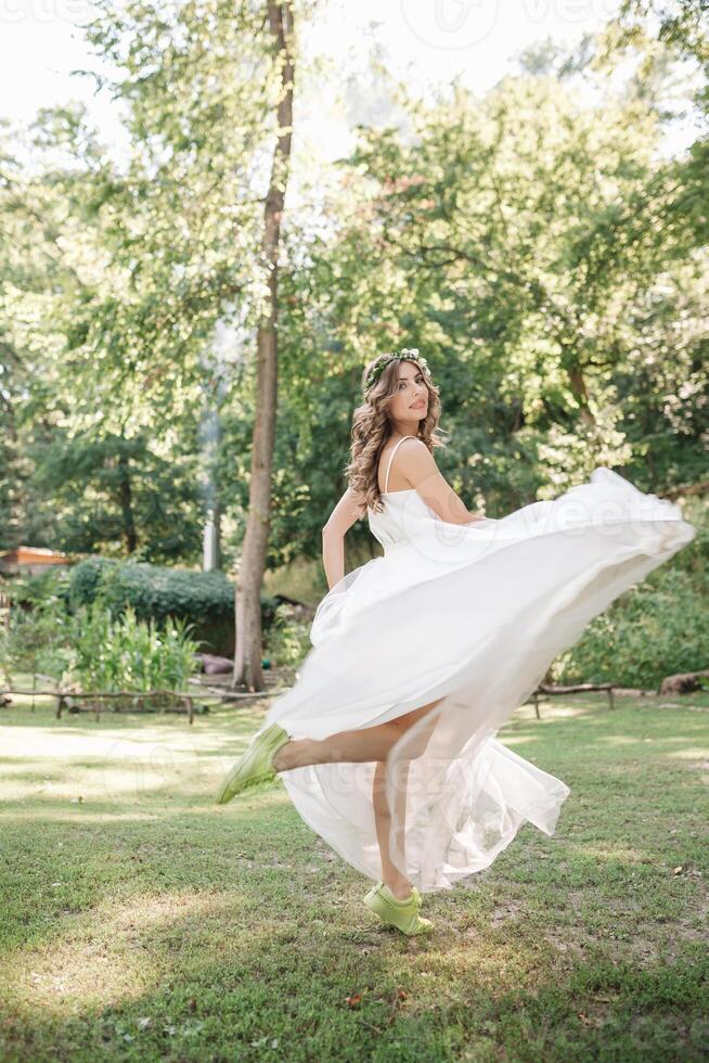 joven niña en un blanco vestir en el prado. mujer en un hermosa largo vestir posando en el jardín. maravilloso novia en un Boda vestir foto