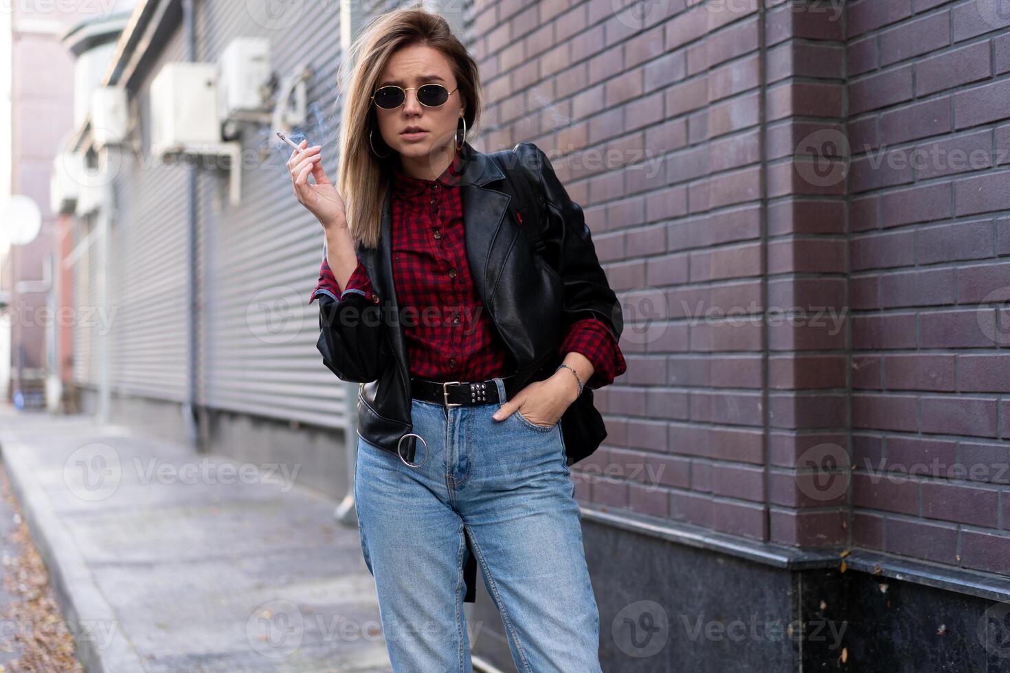 hermosa joven elegantemente vestido caucásico niña fuma cigarrillo en el calle. foto