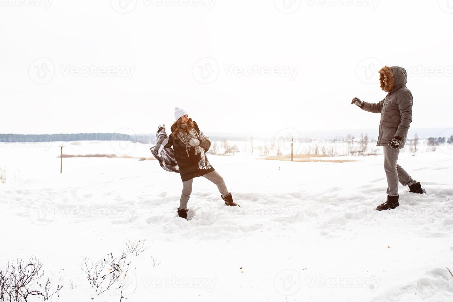 Carefree happy young couple having fun together in snow in winter woodland throwing snowballs at each other during a mock fight photo