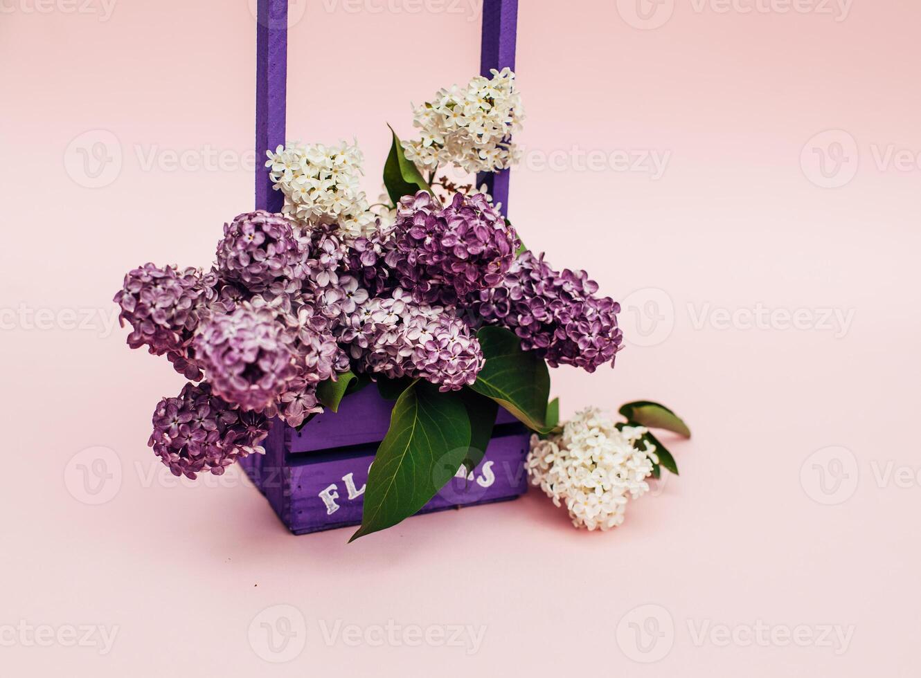 Lilac flowers bunch in a violet wooden basket over pink background. Beautiful violet Lilac flower still life Easter border design on wooden table. Beauty fragrant Lilac Flowers bouquet with Copy space photo