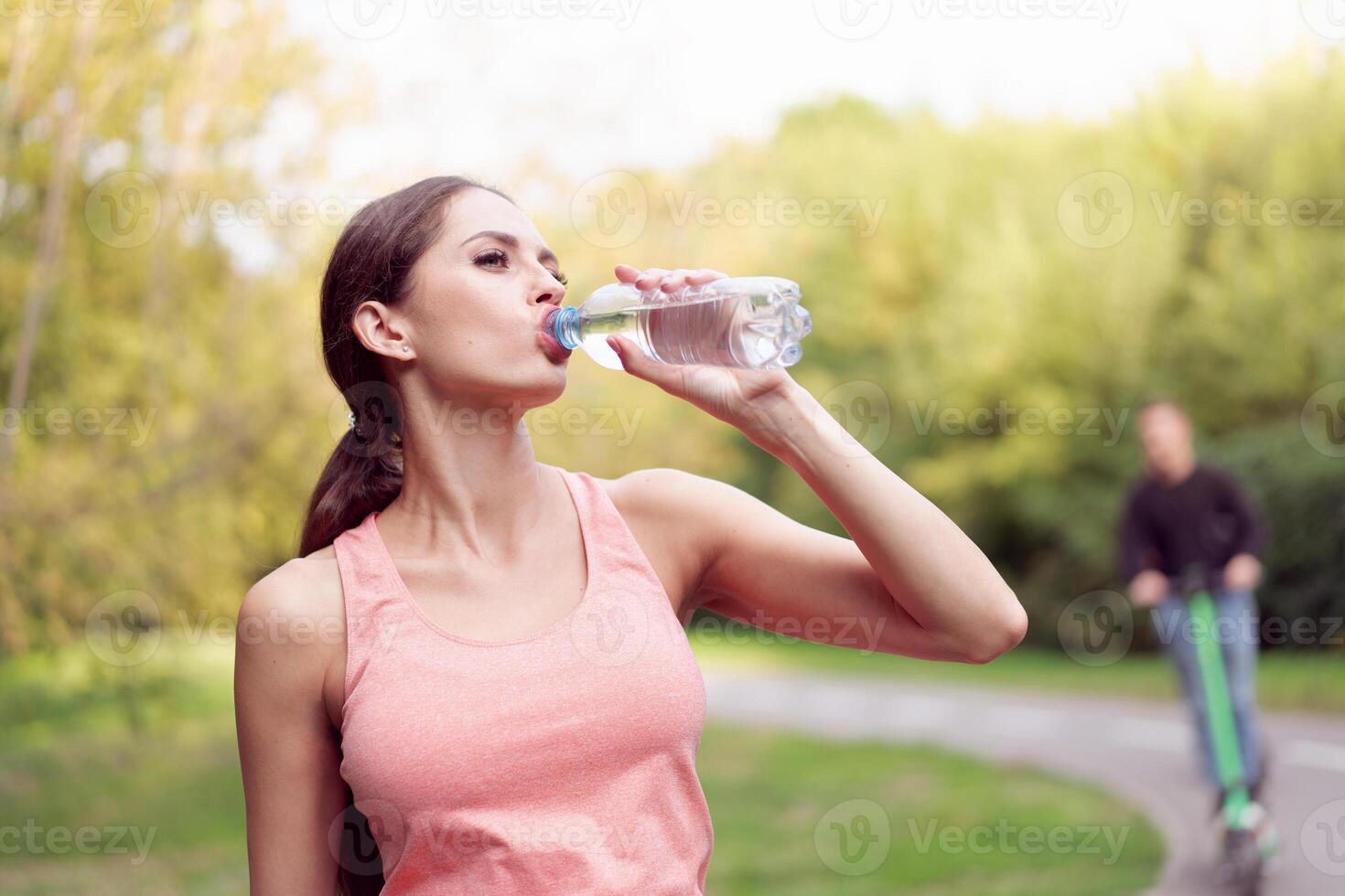 Athletic woman standing running track in summer park drink water after running exercises photo