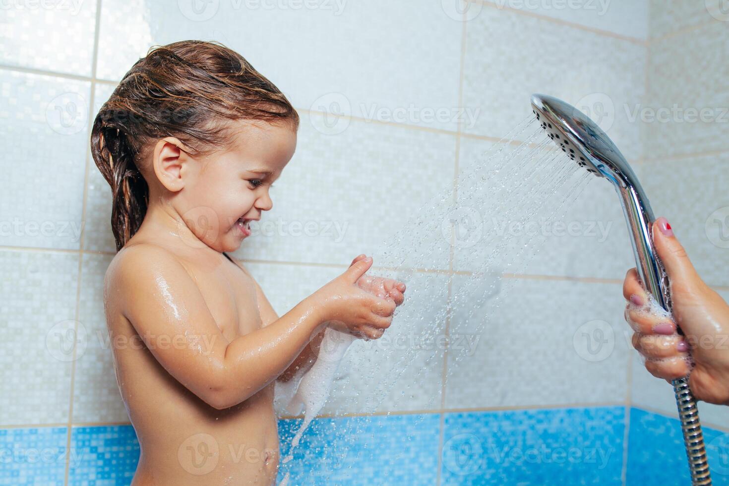 hermosa pequeño niña tomando un baño. un niño es jugado con agua y rociar desde el ducha. alegre para niños higiene. travieso hija en el baño foto