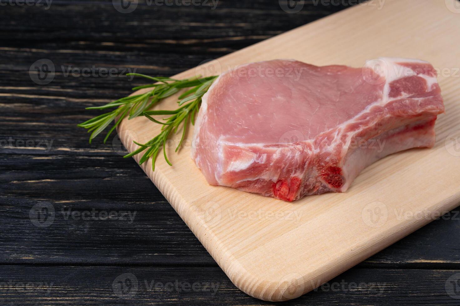 Top view of one pieces raw pork chop steaks with rosemary on a cutting board. photo