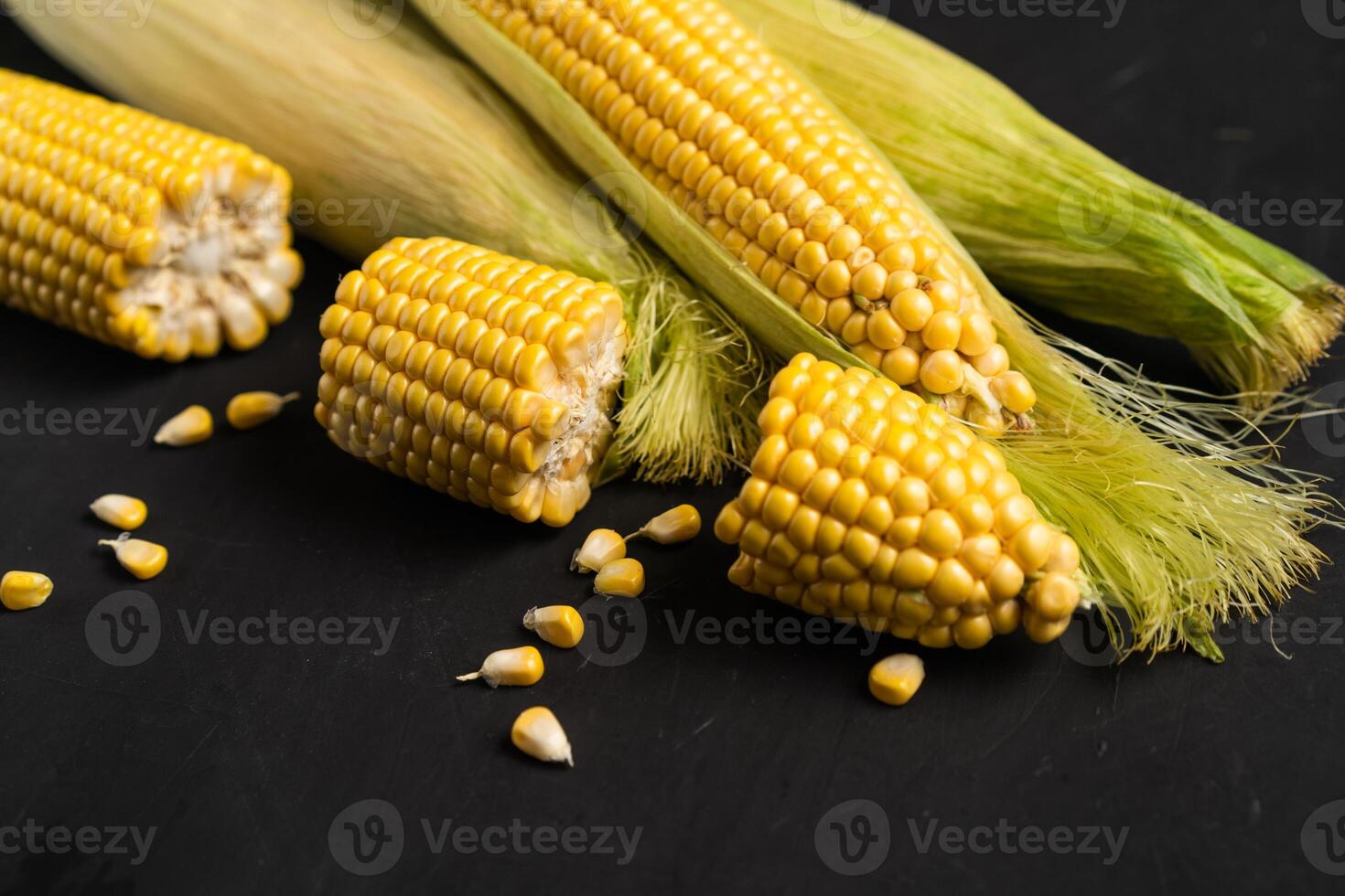 Corn cob with green leaves lies on table black color background. photo