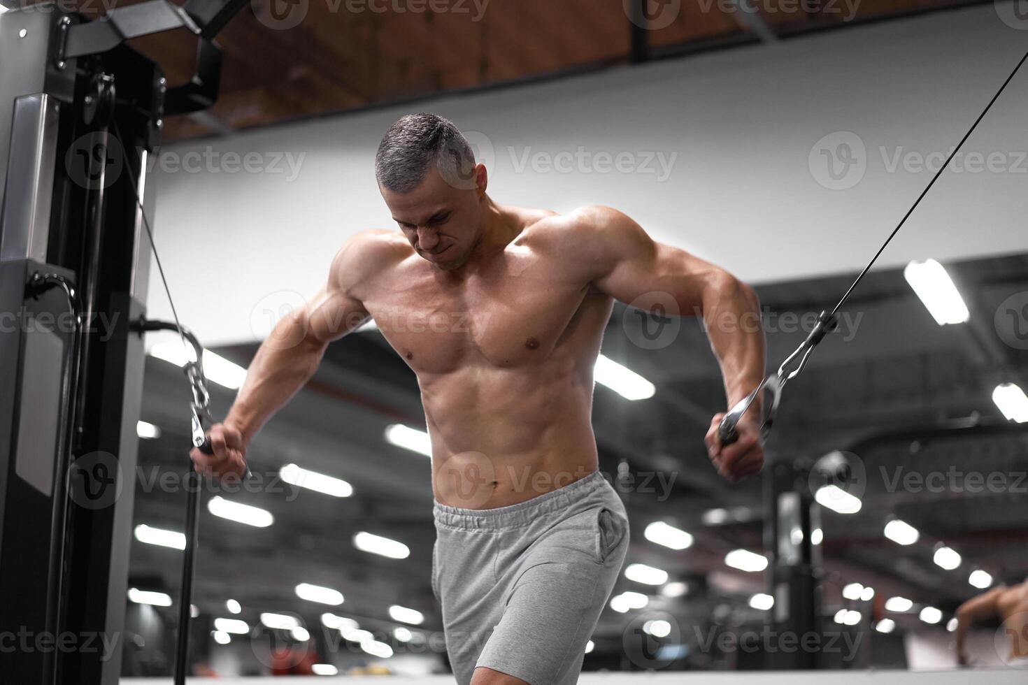Muscular athletic bodybuilder standing training chest and shoulders muscles on fitness equipment photo