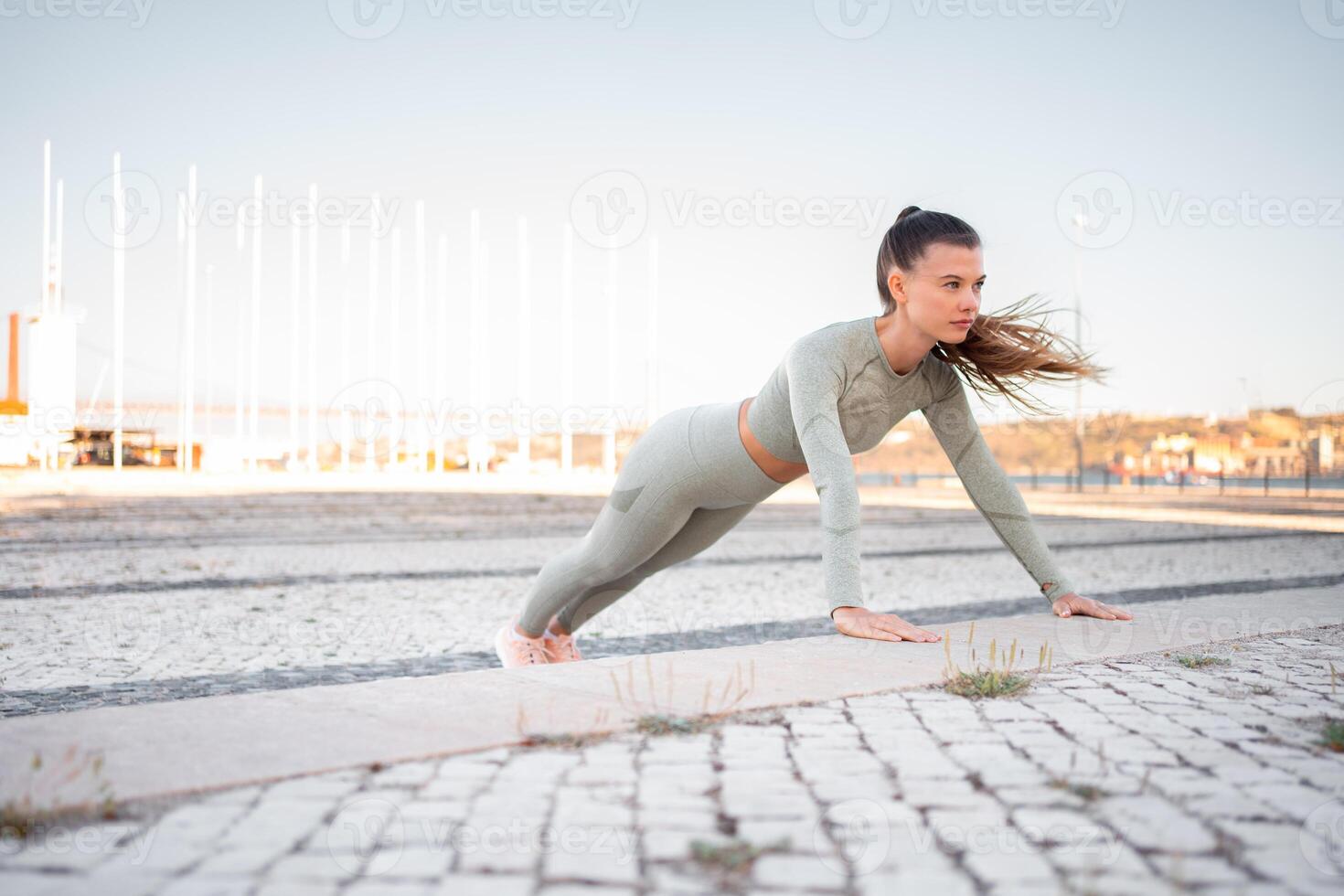 Young attractive girl athlete in sportswear performing push-ups on concrete step photo