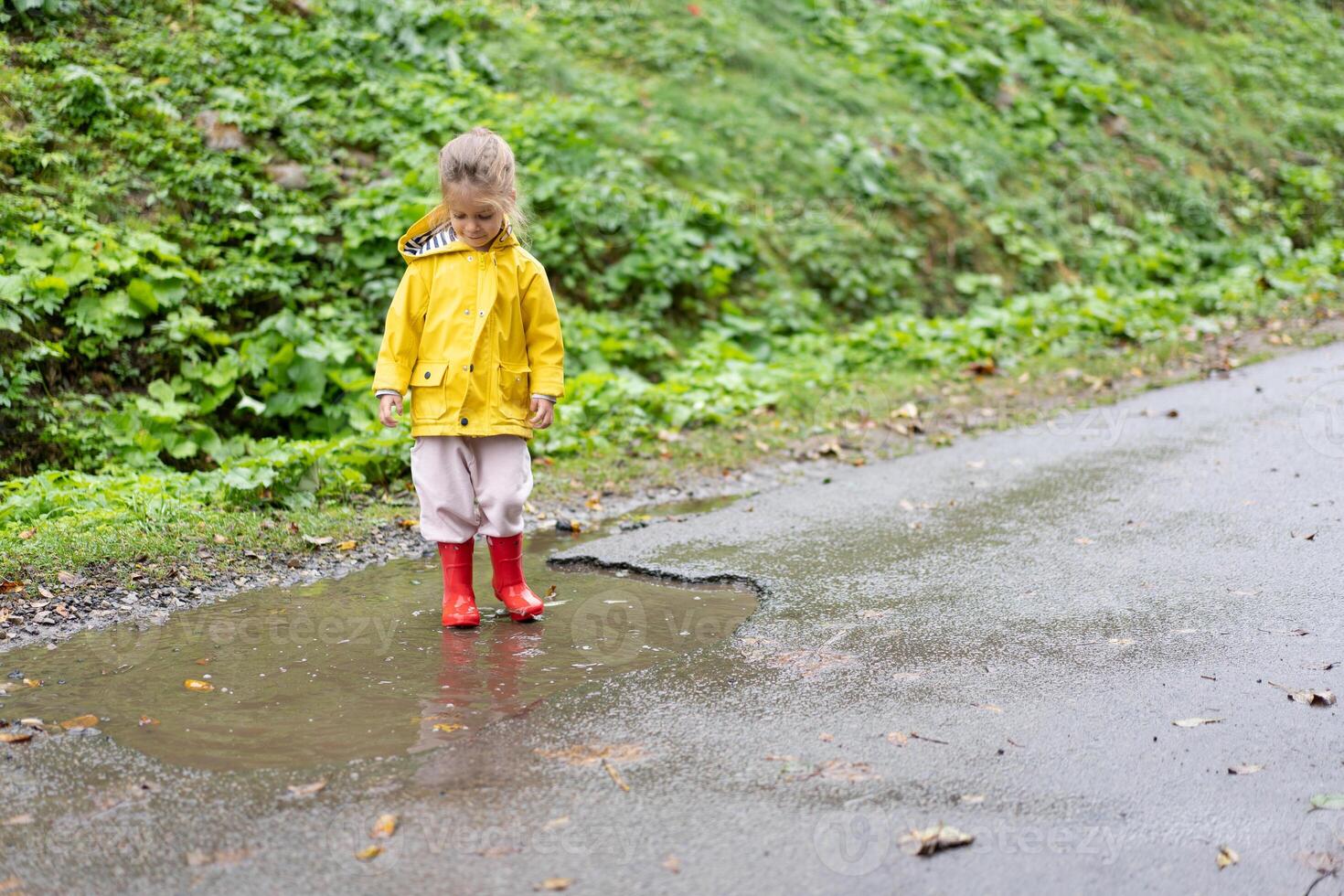 Playful girl wearing yellow raincoat while jumping in puddle during rainfall photo