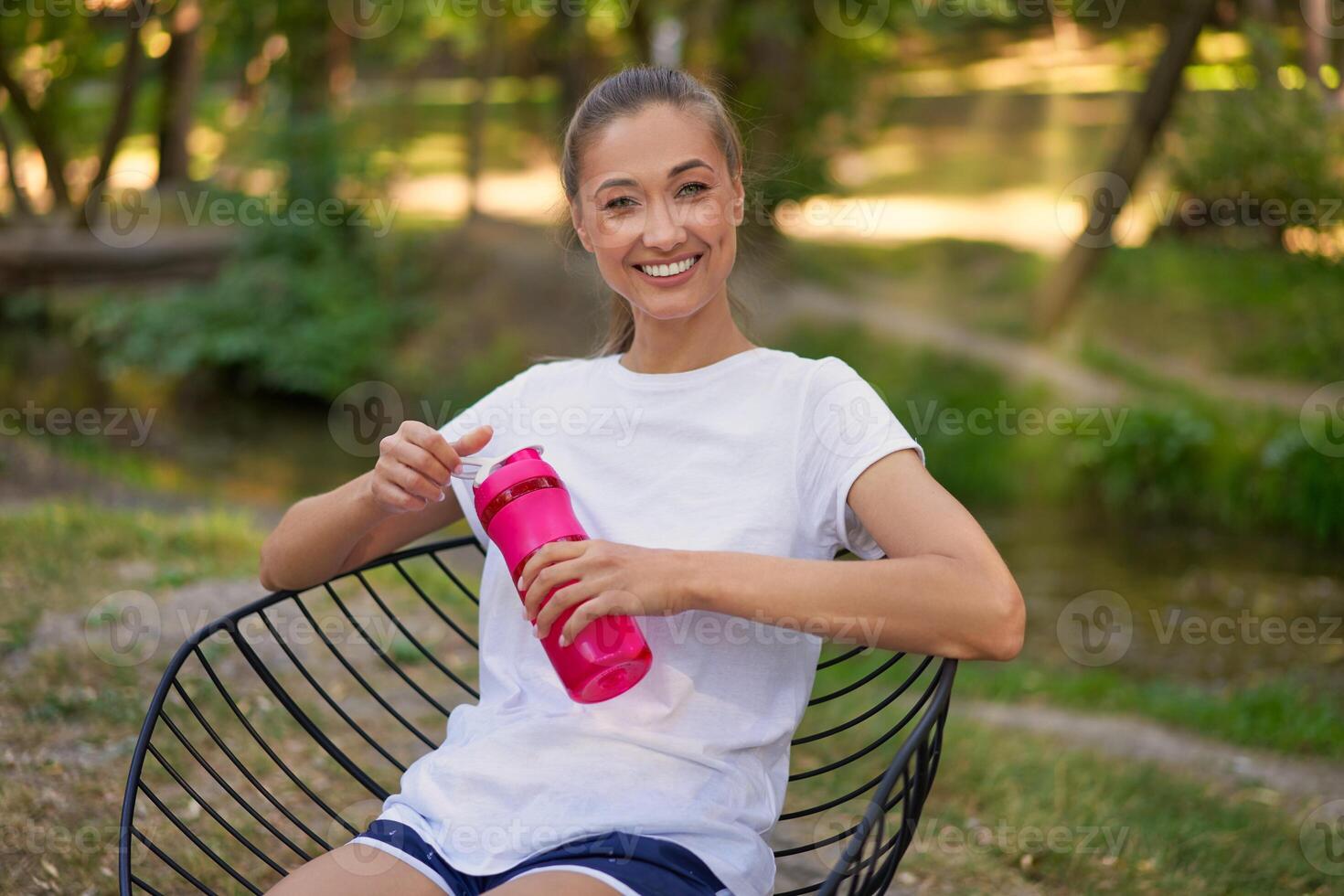 Woman itting chair drink water red bottle after morning workout. photo