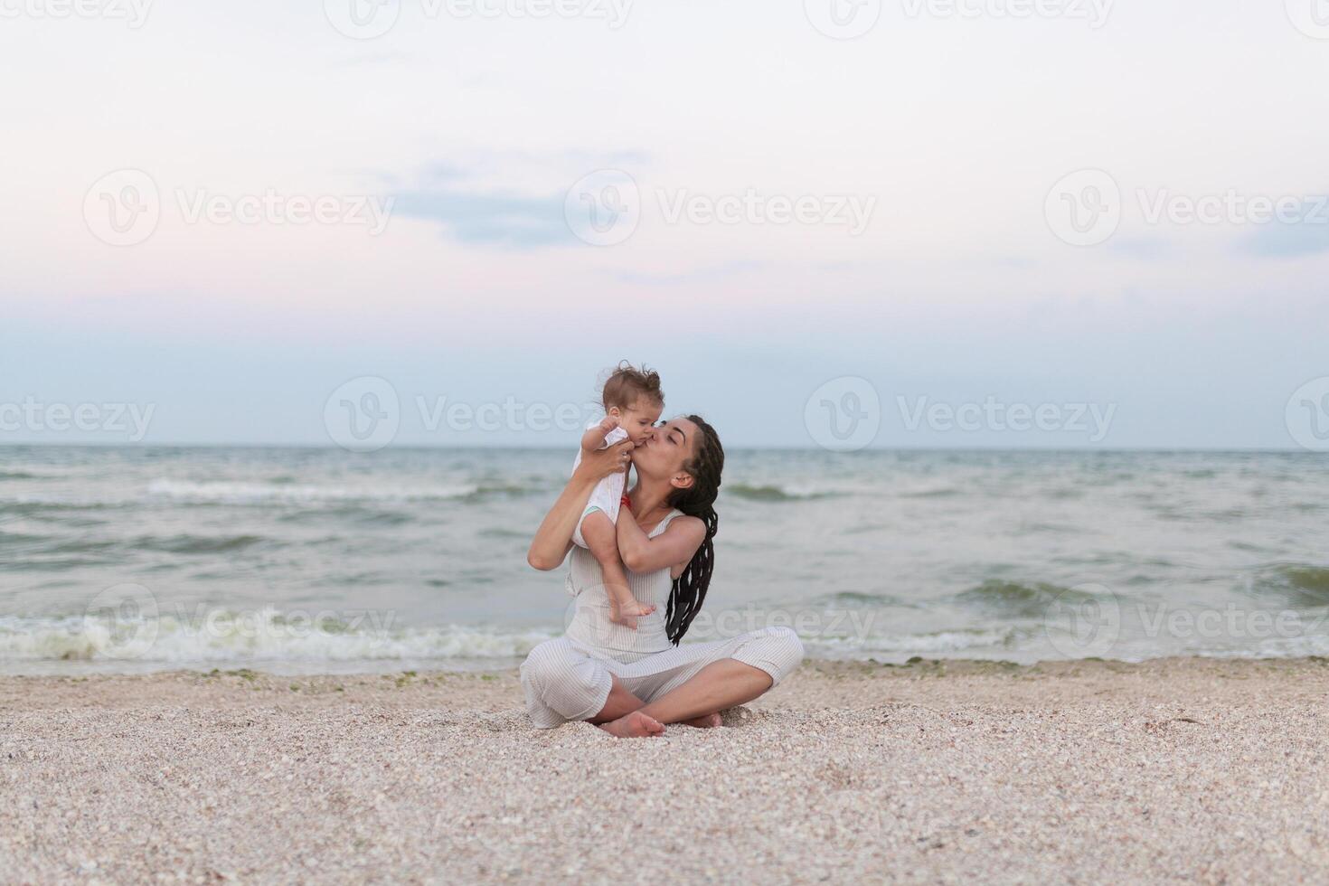 Happy family mother and child daughter doing yoga, meditate in lotus position on beach at sunset photo