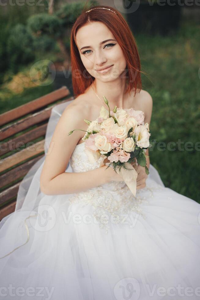 Bride in elegant wedding gown sits on stone bench photo